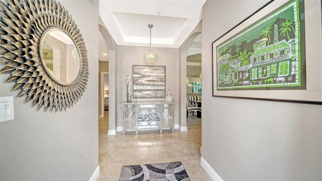 A foyer features a sunburst mirror, a mirrored console table, and a framed green print — 7552 DIVOT LOOP, BRADENTON, FL