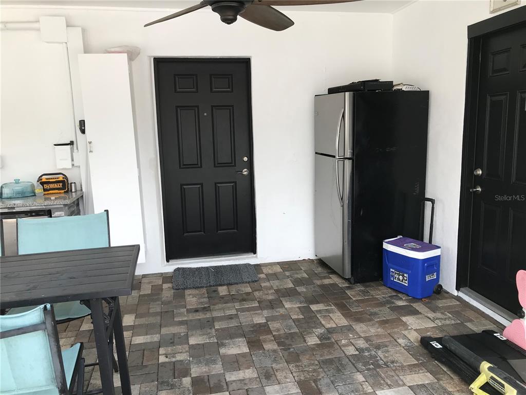 A covered patio features a tiled floor, two black doors, and a stainless steel refrigerator — 6908 N 21ST STREET, TAMPA, FL