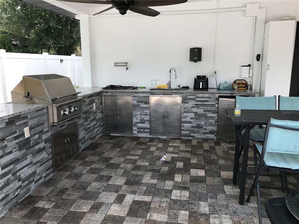 An outdoor kitchen features a stainless steel grill, sink, stone-tiled cabinetry, and a dining set — 6908 N 21ST STREET, TAMPA, FL