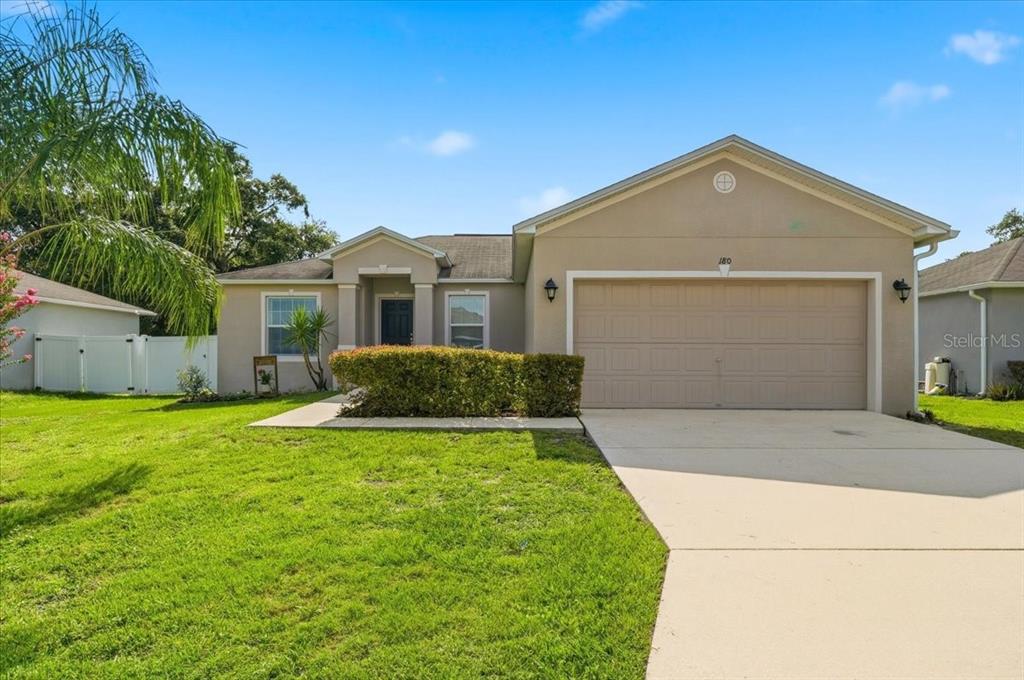 A single-story house with a beige stucco exterior, a two-car garage, and a front lawn — 180 SOLIS DRIVE, WINTER HAVEN, FL