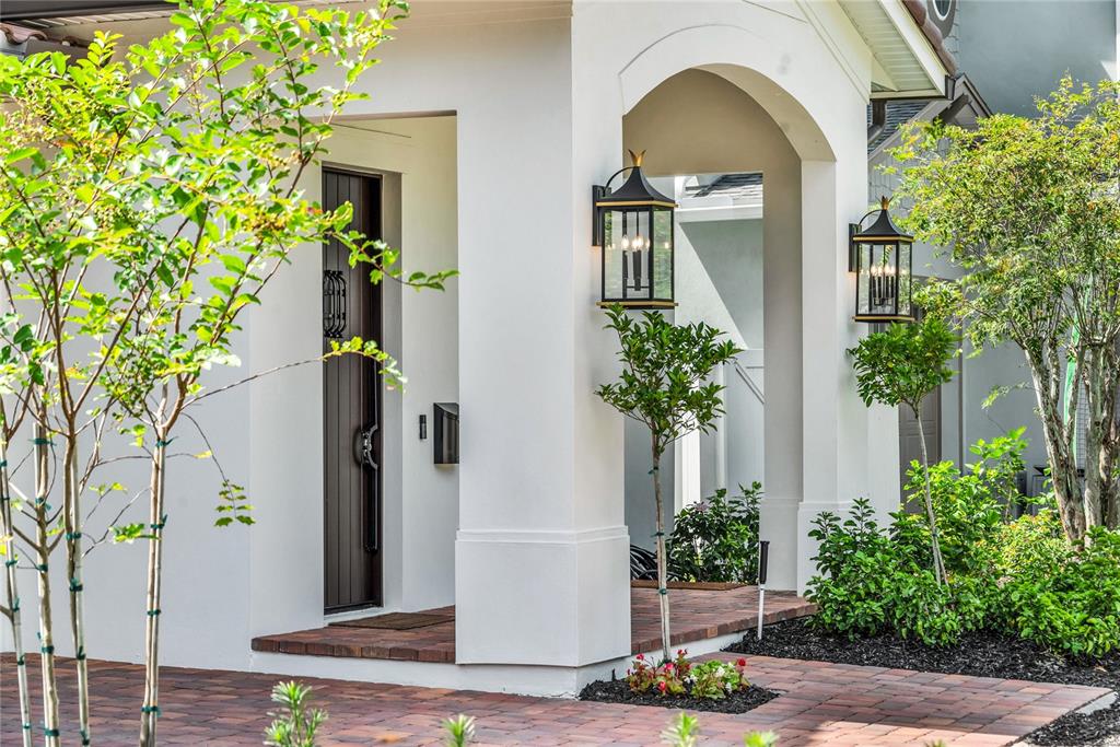 A white arched entryway features a dark wood door, brick flooring, and two wall-mounted lanterns — 1430 STETSON STREET, ORLANDO, FL