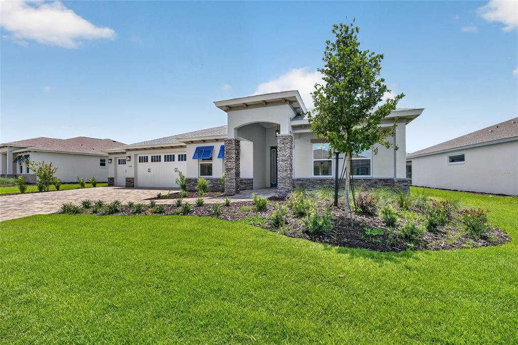 A single-story house with a stone-accented entryway, a three-car garage, and blue window shutters — 10222 SW 84TH STREET ROAD, OCALA, FL
