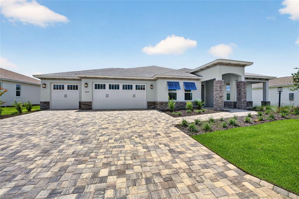A single-story house with a paved driveway, three-car garage, and blue window awnings — 10222 SW 84TH STREET ROAD, OCALA, FL