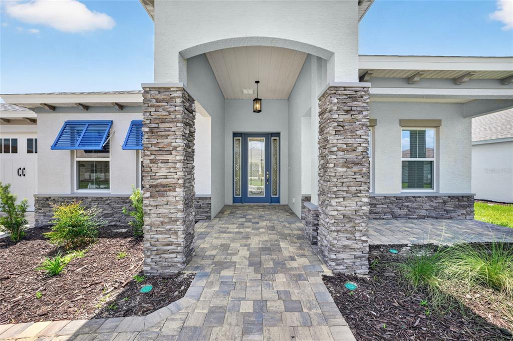 The exterior of a house features a stone-pillared entryway, blue shutters, and a paver walkway — 10222 SW 84TH STREET ROAD, OCALA, FL