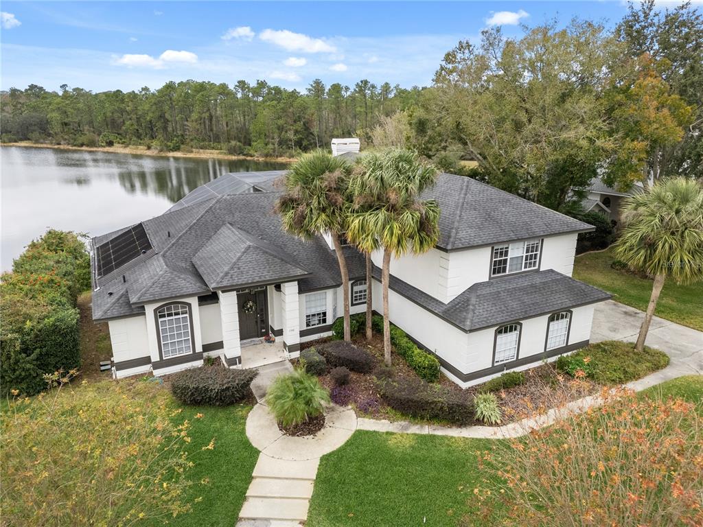 An aerial view shows a two-story white house with a dark roof beside a lake — 1746 CARILLON PARK DRIVE, OVIEDO, FL