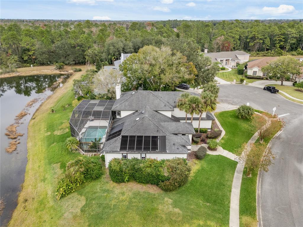 An aerial view shows a house with a screened pool, solar panels, and a pond — 1746 CARILLON PARK DRIVE, OVIEDO, FL
