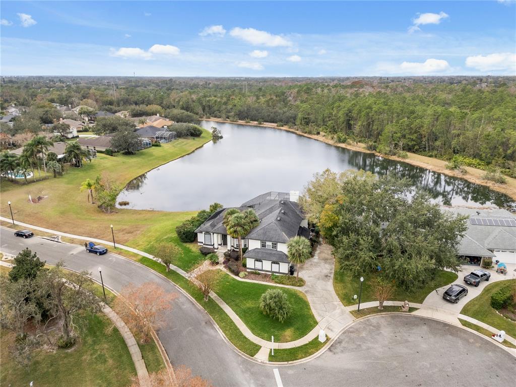 An aerial view shows a house with a dark roof situated on a lakefront lot — 1746 CARILLON PARK DRIVE, OVIEDO, FL