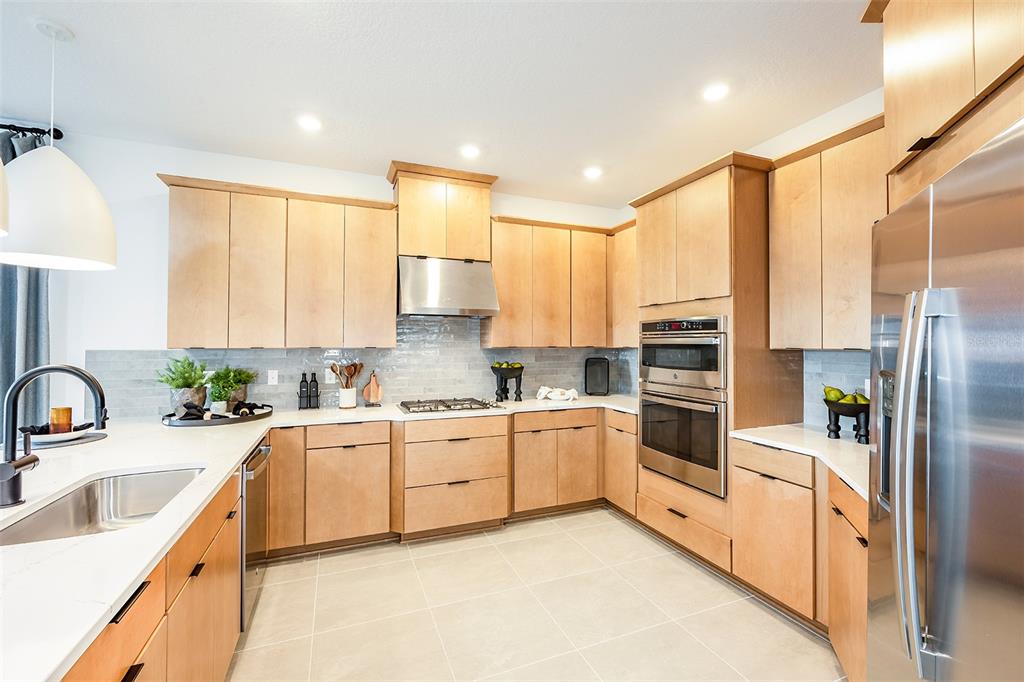 A modern kitchen features light wood cabinets, stainless steel appliances, and white quartz countertops — 19337 LOCHSIDE LANE, MOUNT DORA, FL