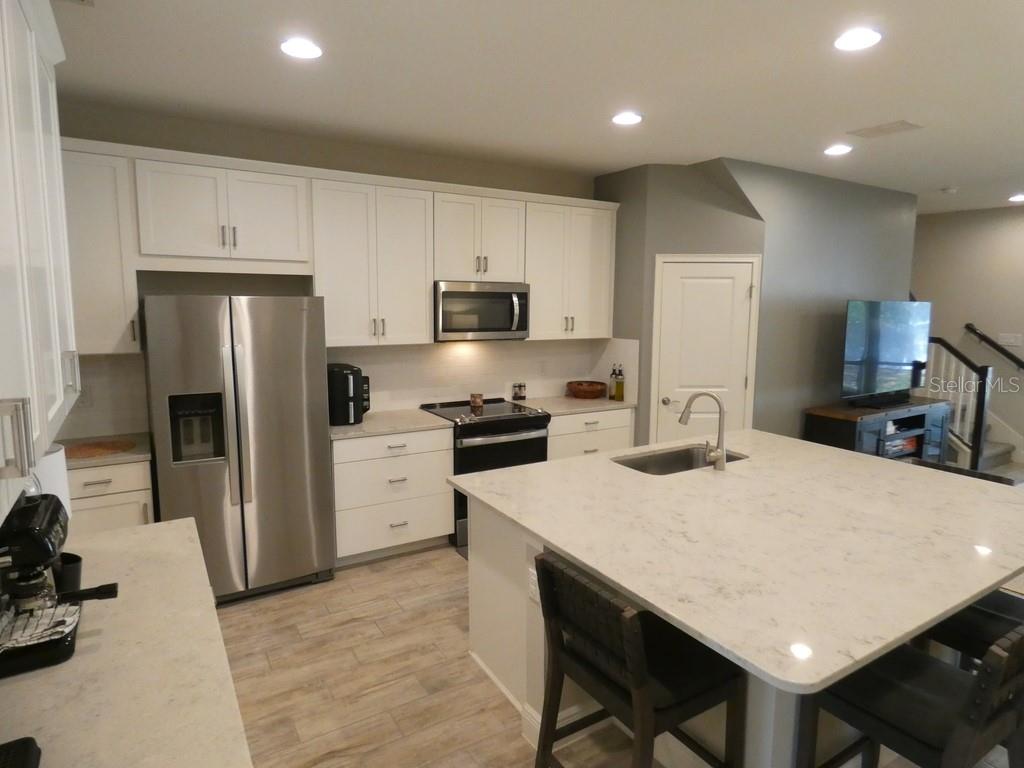 A modern kitchen features white cabinets, stainless steel appliances, and a large quartz-topped island — 1505 SUNSET WIND LOOP, OLDSMAR, FL