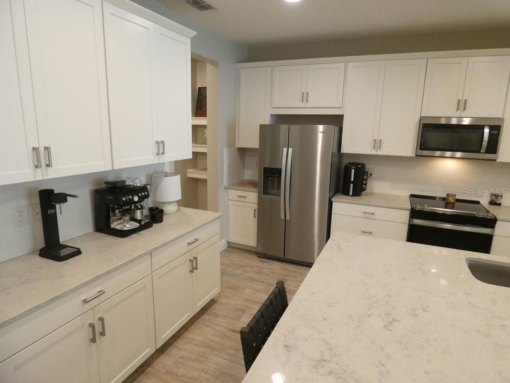 A kitchen features white cabinets, stainless steel appliances, and a large quartz-topped island — 1505 SUNSET WIND LOOP, OLDSMAR, FL