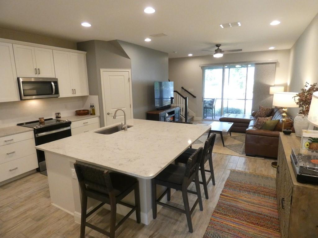 An open-concept kitchen with a large quartz island overlooks a living room and patio — 1505 SUNSET WIND LOOP, OLDSMAR, FL
