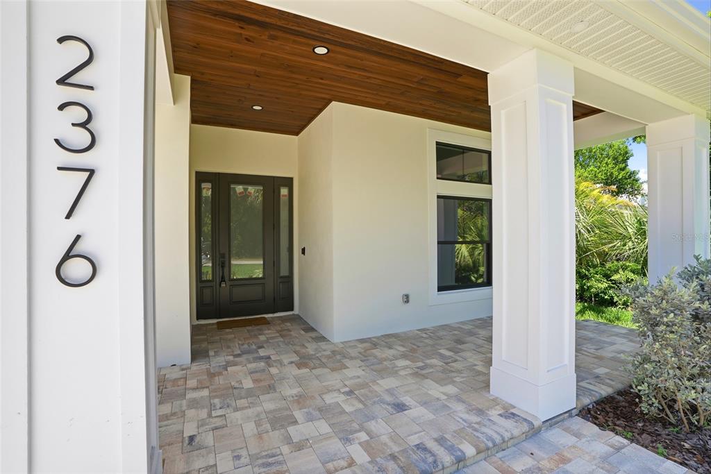 A covered front porch with a wood-paneled ceiling, paver flooring, and a dark glass door — 2376 RAJEL AVENUE, SAFETY HARBOR, FL