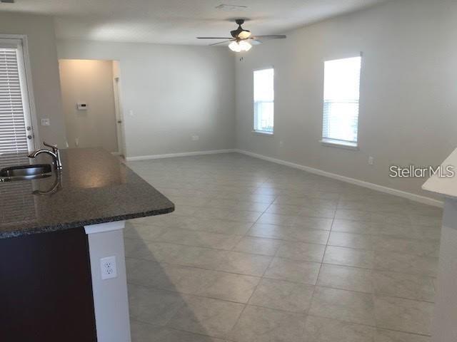 An open-concept living area features light-colored tile flooring, a ceiling fan, and a kitchen island — 6168 GLORY BOWER DRIVE, WINTER GARDEN, FL