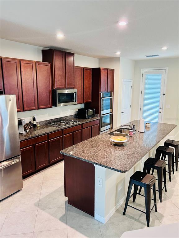 A kitchen features dark wood cabinets, granite countertops, a center island, and stainless steel appliances — 6168 GLORY BOWER DRIVE, WINTER GARDEN, FL