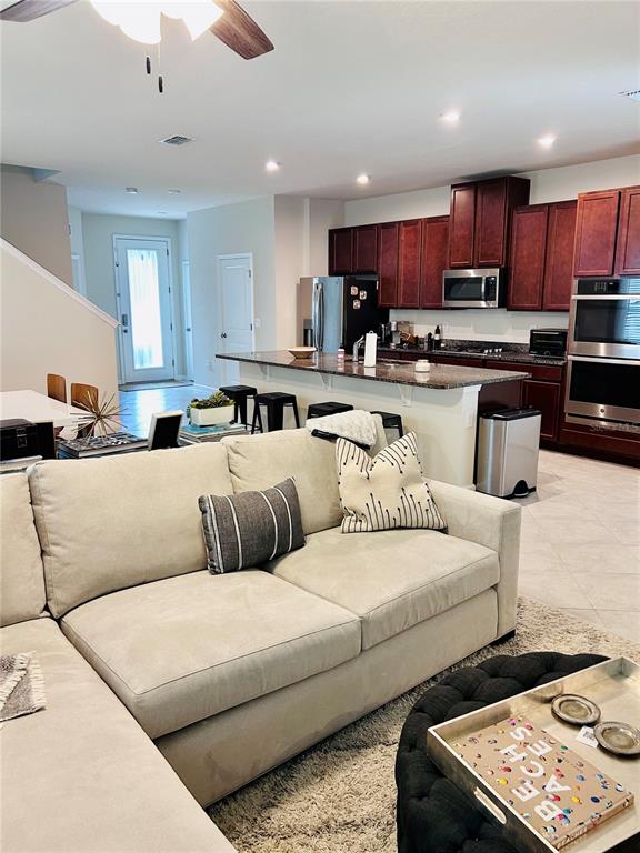 An open-concept living room features a beige sectional sofa facing a kitchen with dark wood cabinets — 6168 GLORY BOWER DRIVE, WINTER GARDEN, FL