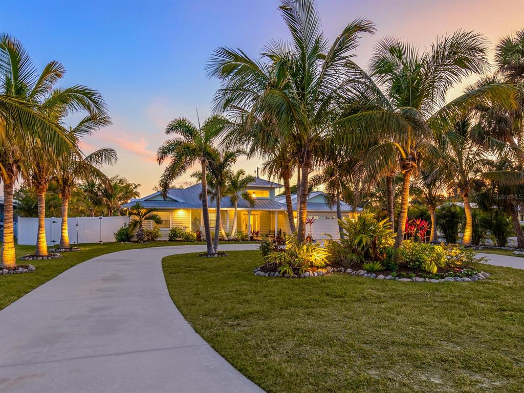 A single-story house with a curved driveway and palm trees at sunset — 221 LYCHEE ROAD, NOKOMIS, FL