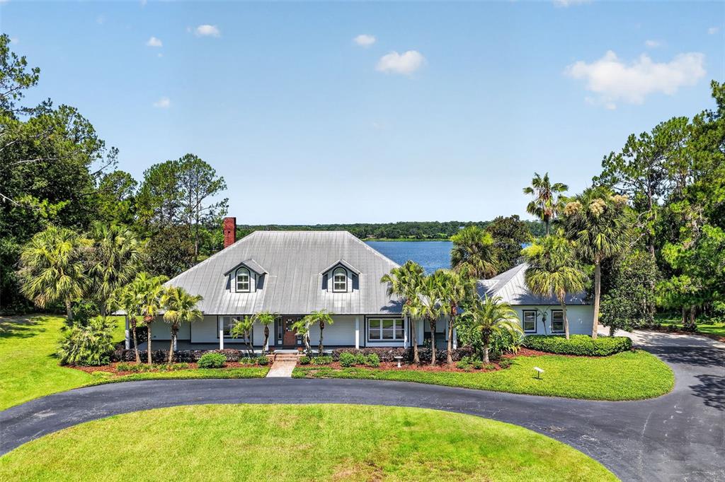 A white house with a metal roof and dormer windows sits beside a lake — 22625 LAKE SENECA ROAD, EUSTIS, FL