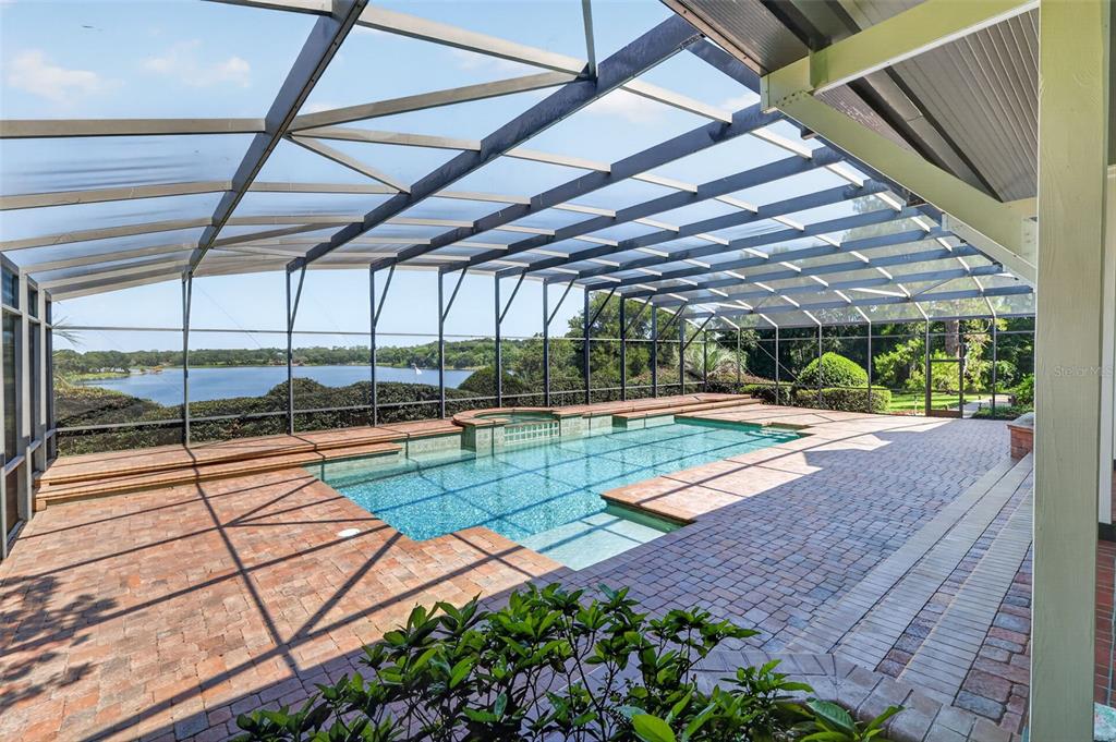 A screened-in patio features a rectangular swimming pool with a spa overlooking a lake — 22625 LAKE SENECA ROAD, EUSTIS, FL