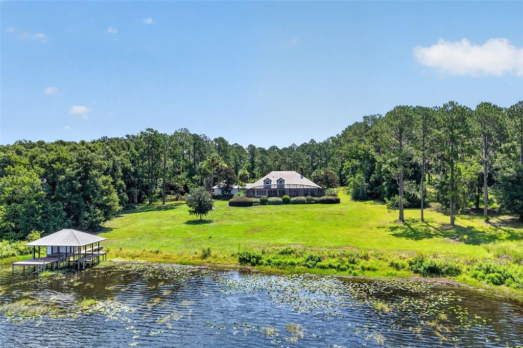 A house with a screened porch sits on a grassy hill overlooking a lake dock — 22625 LAKE SENECA ROAD, EUSTIS, FL