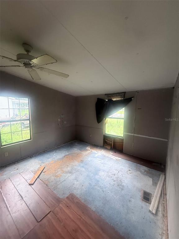 An unfinished room features exposed subflooring, bare wall panels, a ceiling fan, and two windows — 13114 SE 32ND COURT, BELLEVIEW, FL