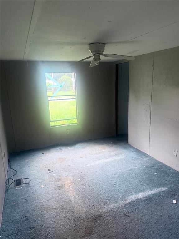 An empty bedroom features blue carpeting, paneled walls, a ceiling fan, and a single window — 13114 SE 32ND COURT, BELLEVIEW, FL