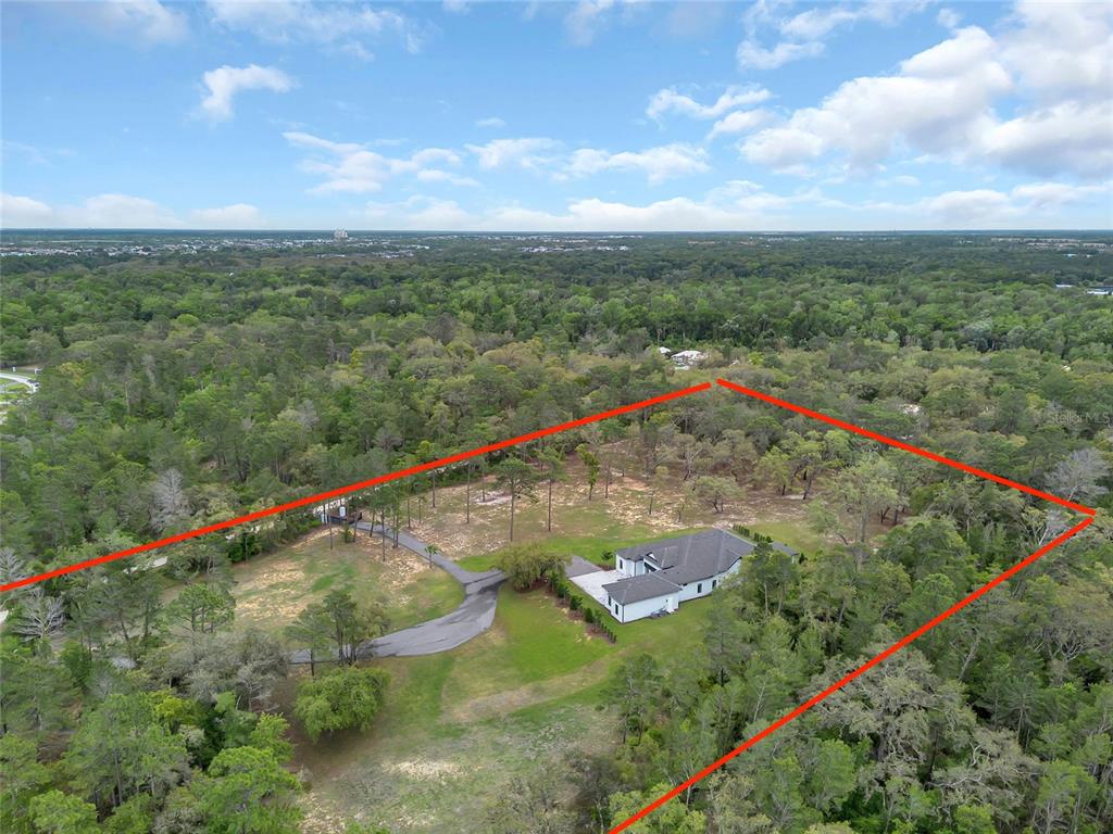 An aerial view shows a house situated on a large, wooded lot with red boundary lines — 8398 HAPPY TRAIL, KISSIMMEE, FL