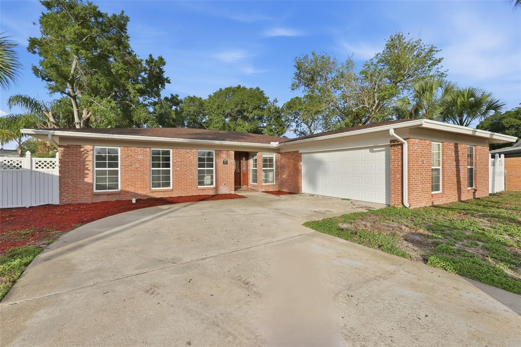 A single-story brick house features a concrete driveway, palm trees, and white vinyl fencing — 8410 LAVA PLACE, TAMPA, FL