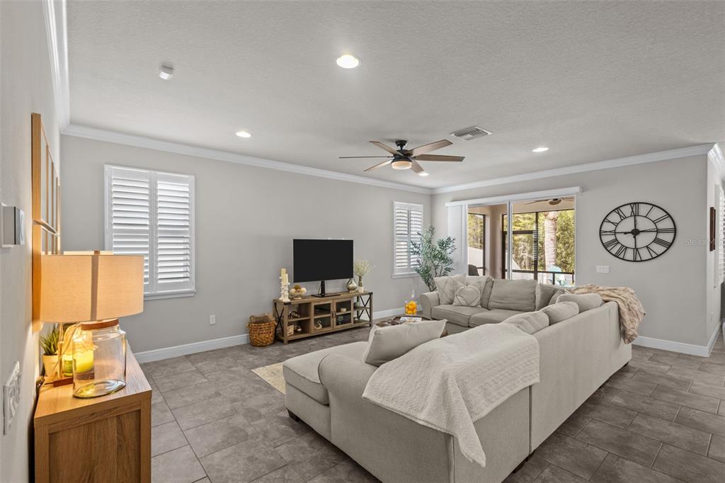 A living room features a large sectional sofa, a television on a console, and tile flooring — 14426 TRAILS EDGE BOULEVARD, ODESSA, FL