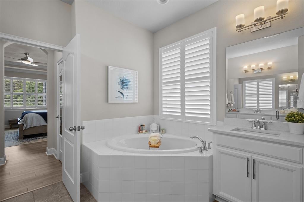 A bathroom features a white corner soaking tub, a vanity with a mirror, and plantation shutters — 14426 TRAILS EDGE BOULEVARD, ODESSA, FL