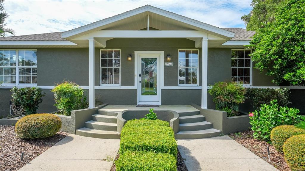 The exterior of a house features a covered front porch with steps and green landscaping — 20368 THE GRANADA, DUNNELLON, FL