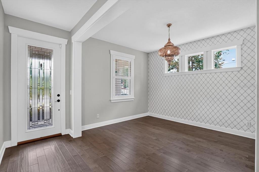 An empty dining room with dark wood floors, patterned wallpaper, and a decorative pendant light — 3615 W RENELLIE CIRCLE, TAMPA, FL