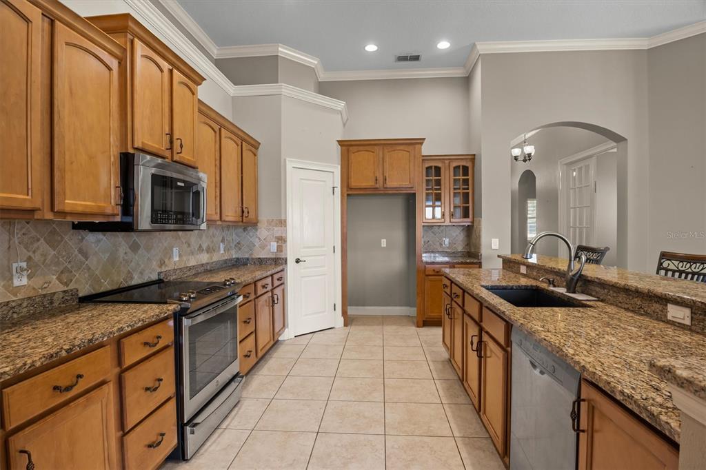 A kitchen features wood cabinets, granite countertops, stainless steel appliances, and tile flooring — 8281 LAKE JAMES DRIVE, LAKELAND, FL