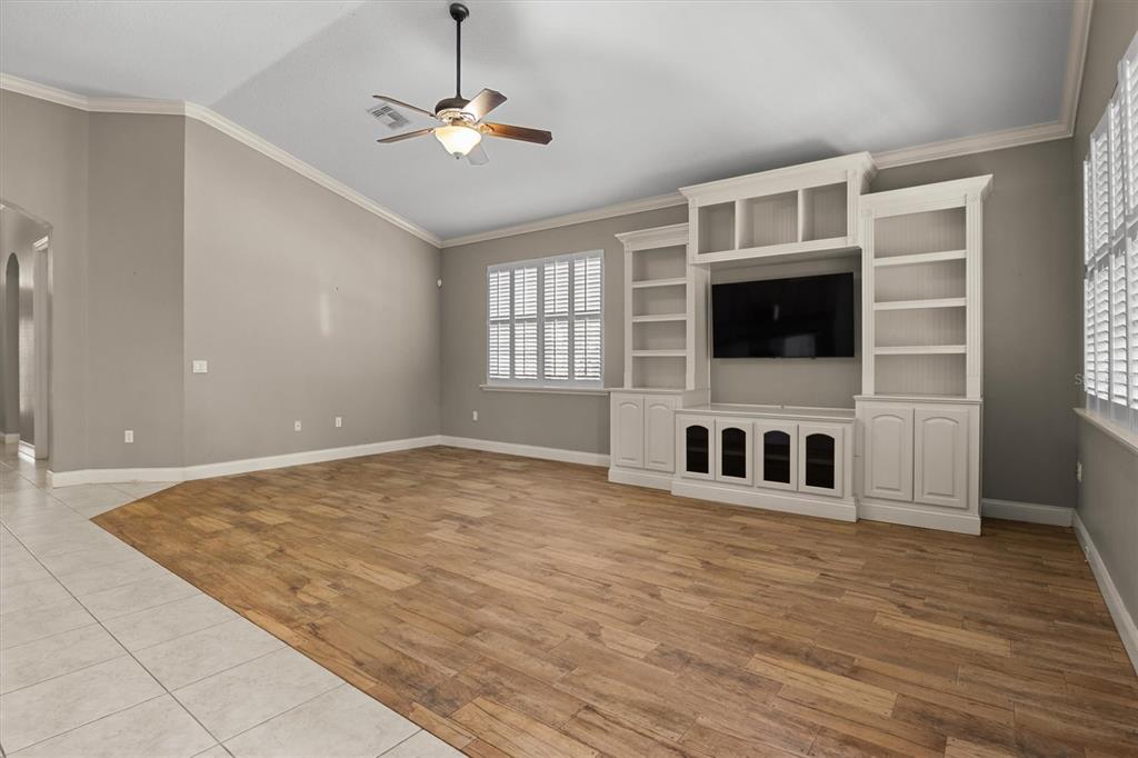 A living room with wood-look flooring, a white built-in entertainment center, and a ceiling fan — 8281 LAKE JAMES DRIVE, LAKELAND, FL