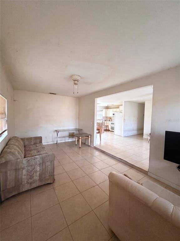 A living room with tiled floors and a sofa leads into an open kitchen area — 1636 SE ARAPAHO AVENUE, STUART, FL