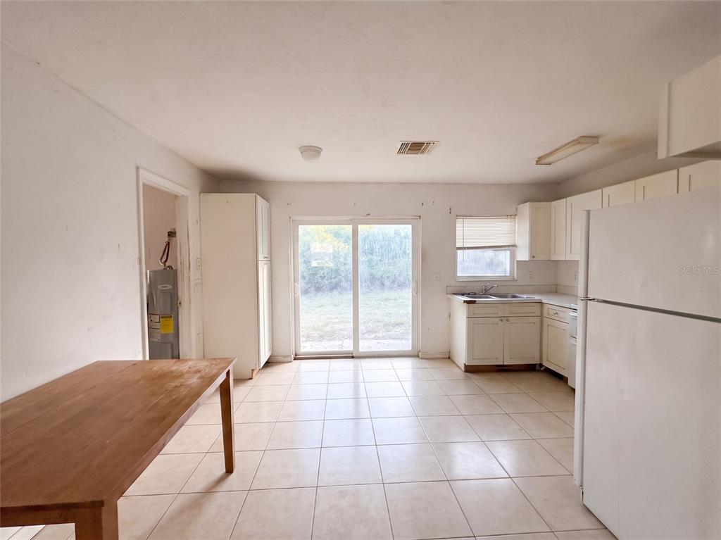 A kitchen with white cabinets, tile flooring, a wooden table, and a sliding glass door — 1636 SE ARAPAHO AVENUE, STUART, FL