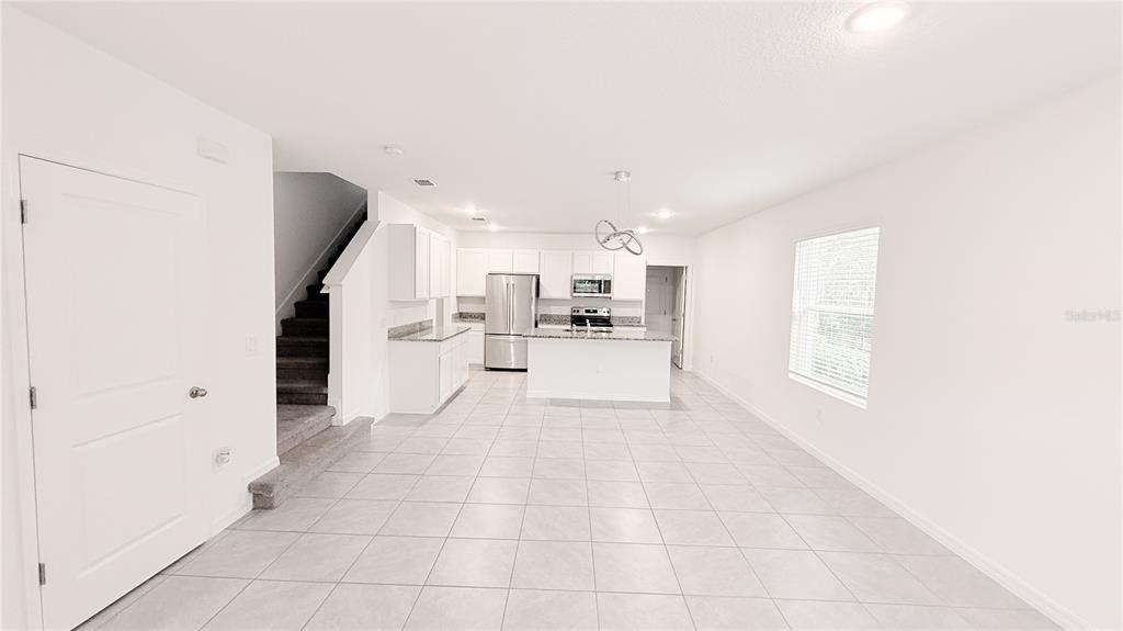An open-concept kitchen and living area features white cabinetry, stainless steel appliances, and tile flooring — 701 COSTA LANE, DEBARY, FL
