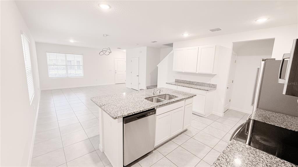 A kitchen with a granite-topped island and white cabinets opens into a tiled living area — 701 COSTA LANE, DEBARY, FL