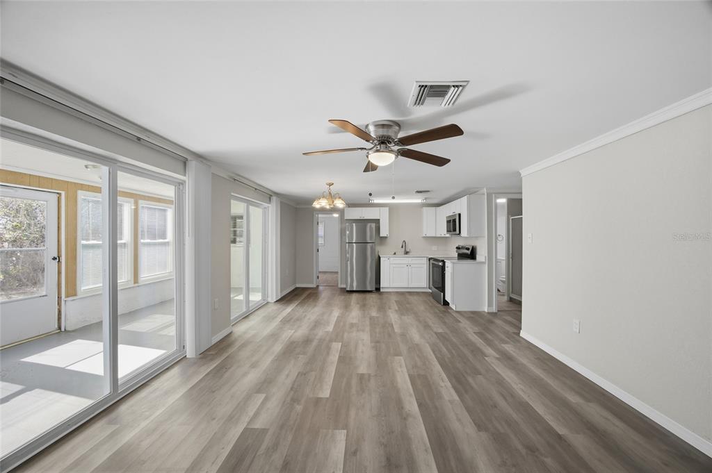 An open-concept living and kitchen area with light wood-look flooring and sliding glass doors — 7410 MAKO DRIVE, HUDSON, FL