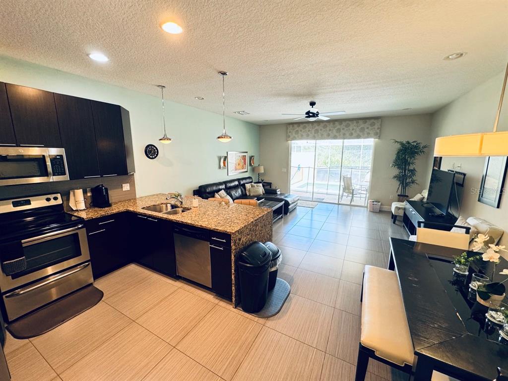 An open-concept kitchen, dining area, and living room with dark cabinetry and tile flooring — 17531 PLACIDITY AVENUE, CLERMONT, FL
