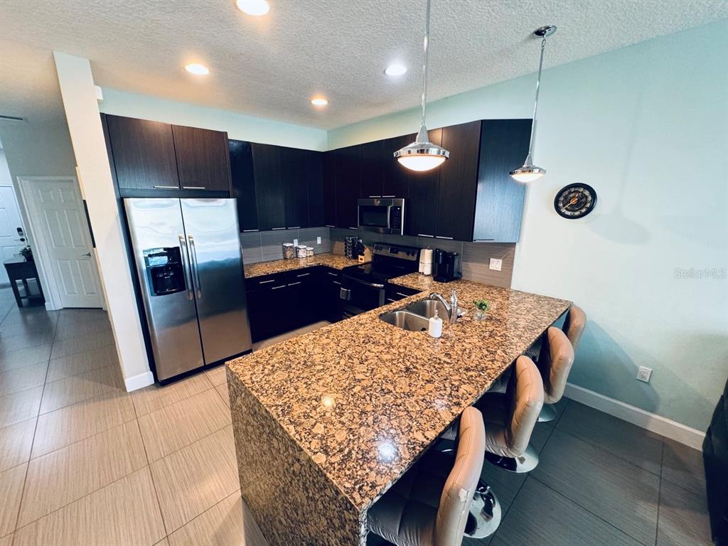 A kitchen features dark wood cabinets, granite countertops, stainless steel appliances, and a breakfast bar — 17531 PLACIDITY AVENUE, CLERMONT, FL