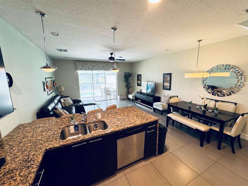 An open-concept kitchen with granite countertops overlooks a living and dining area with tile floors — 17531 PLACIDITY AVENUE, CLERMONT, FL