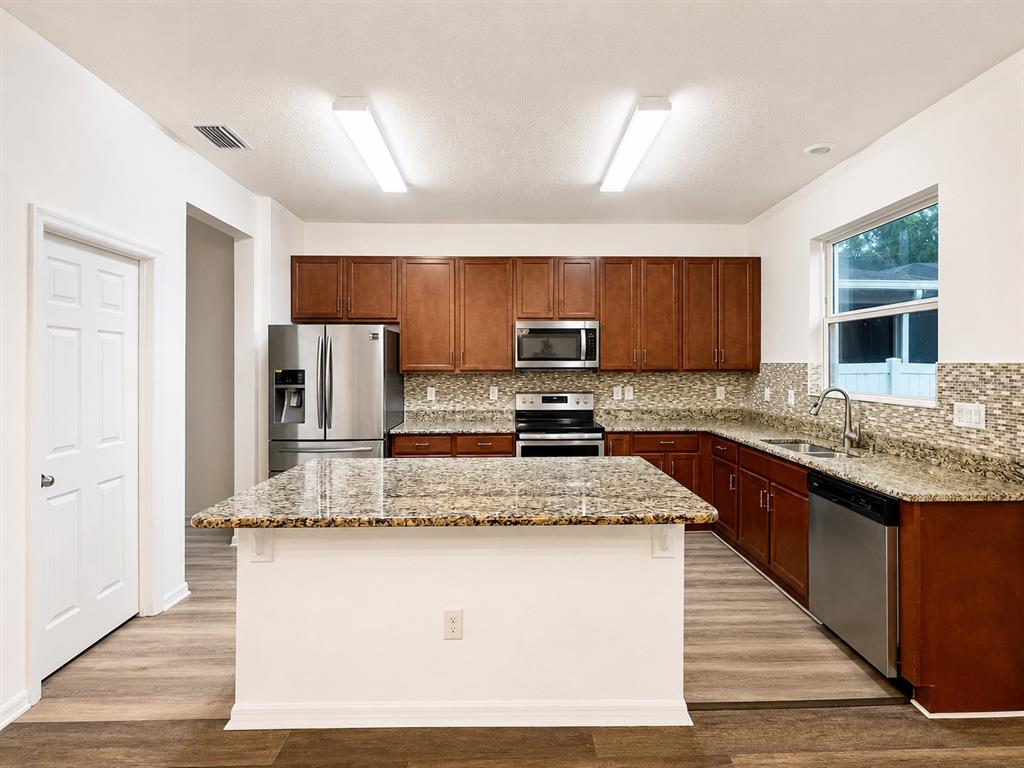 A kitchen features a granite-topped island, stainless steel appliances, and wood-toned cabinetry — 9126 FREEDOM HILL DR, SEFFNER, FL
