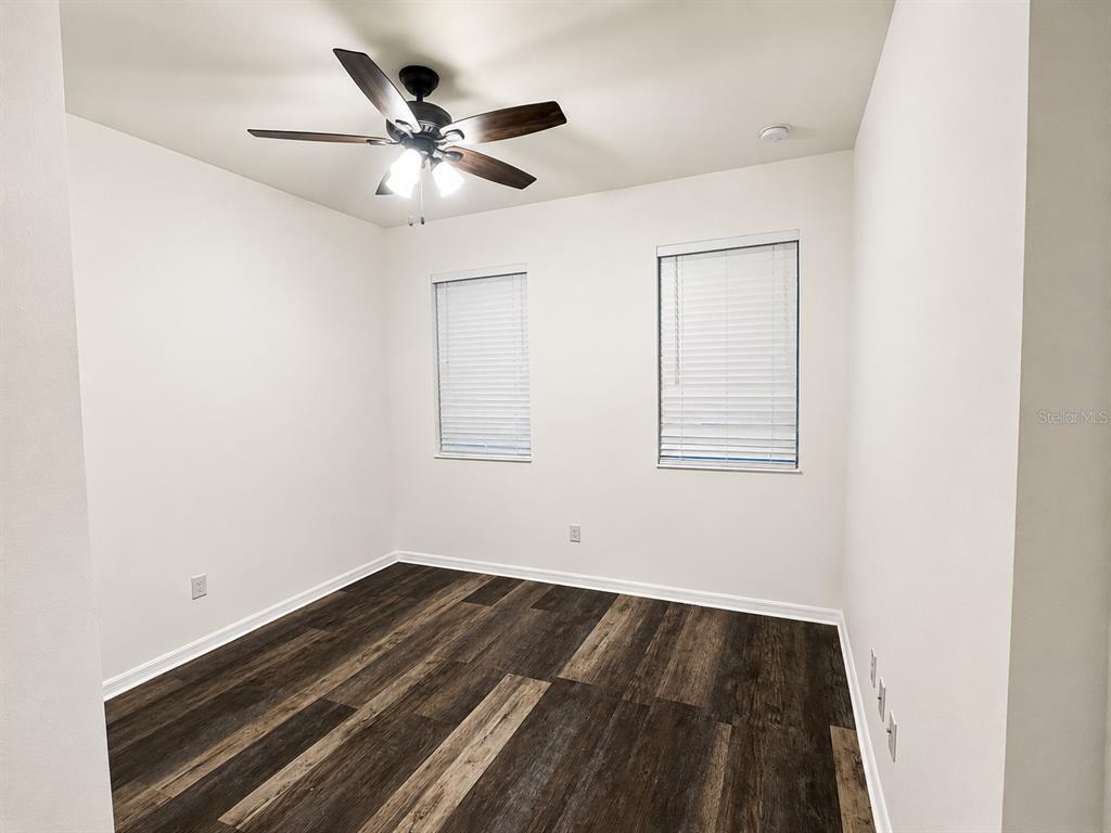 An empty room features white walls, dark wood-look flooring, two windows with blinds, and a ceiling fan — 9126 FREEDOM HILL DR, SEFFNER, FL