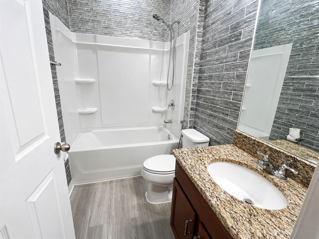 A bathroom features a white tub-shower combo, a granite vanity, and gray tiled walls — 9126 FREEDOM HILL DR, SEFFNER, FL