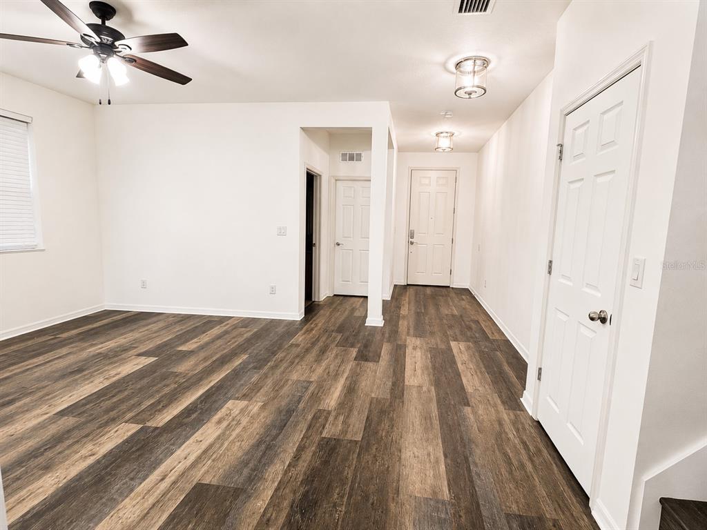 A room with wood-look flooring, a ceiling fan, and white walls leading to an entryway — 9126 FREEDOM HILL DR, SEFFNER, FL