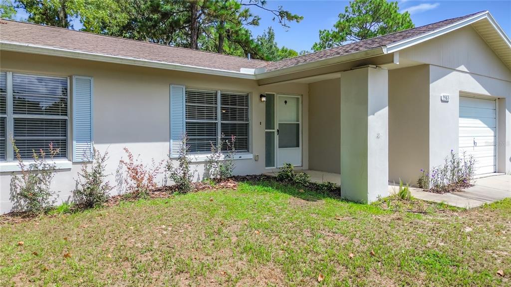 The exterior of a single-story house features a tan stucco facade, a garage, and landscaping — 5583 W CAGNEY LOOP, HOMOSASSA, FL
