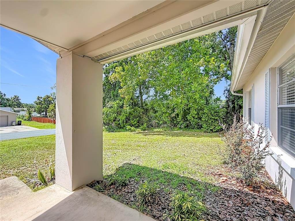 A covered concrete patio overlooks a grassy backyard with trees and a neighboring building — 5583 W CAGNEY LOOP, HOMOSASSA, FL