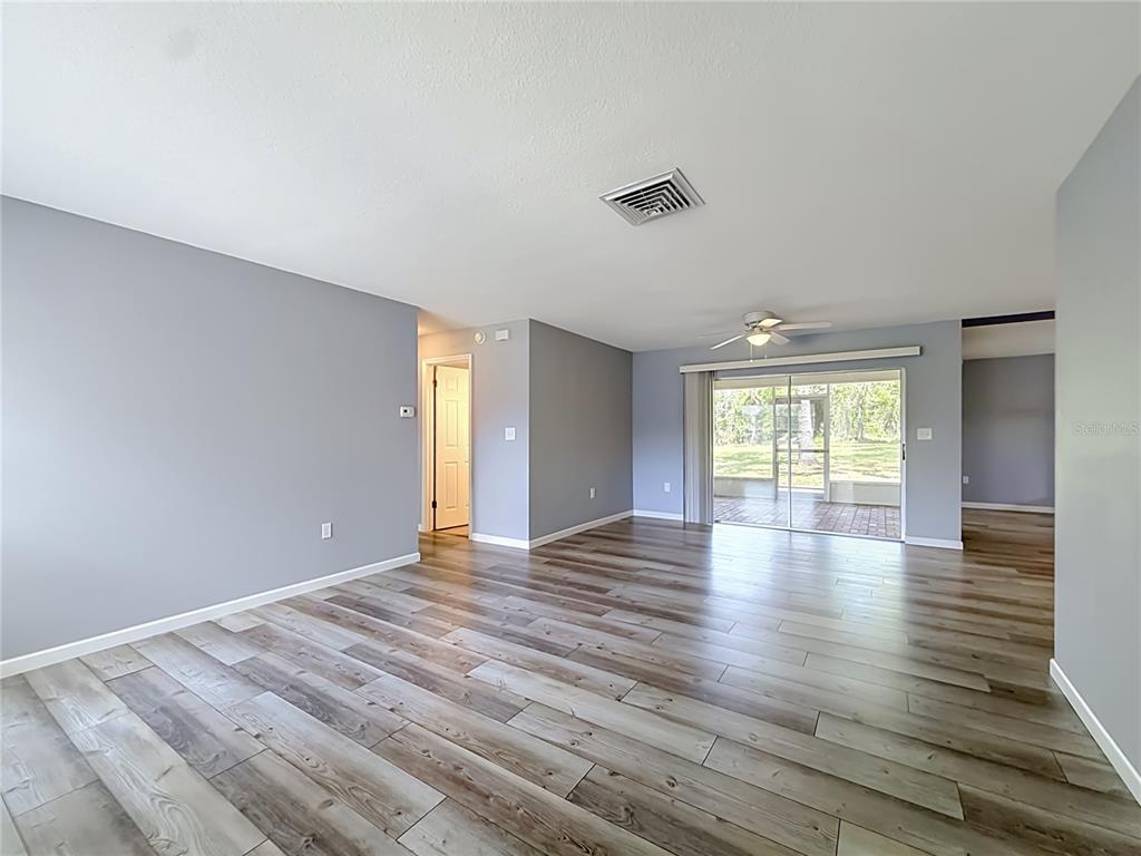 An open living area features gray walls, wood-look flooring, a ceiling fan, and sliding glass doors — 5583 W CAGNEY LOOP, HOMOSASSA, FL
