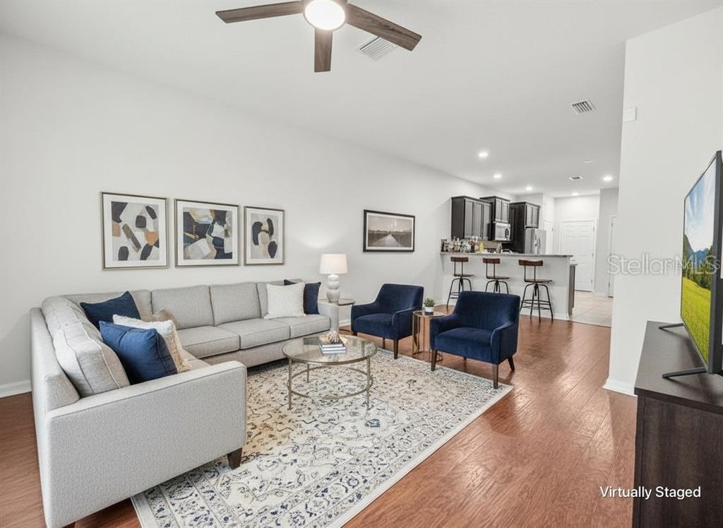 A living room with a gray sectional, two blue armchairs, and an open kitchen area — 9157 HILLCROFT DRIVE, RIVERVIEW, FL