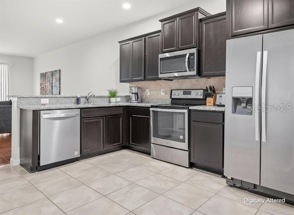 A kitchen features dark wood cabinets, granite countertops, stainless steel appliances, and light tile flooring — 9157 HILLCROFT DRIVE, RIVERVIEW, FL